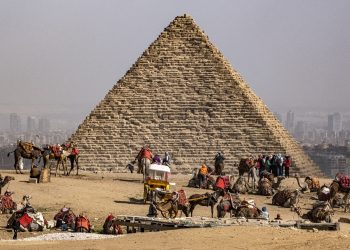 In this picture taken on February 6, 2023, camel guides wait with their animals near the Pyramid of Menkaure (Menkheres) at the Giza Pyramids necropolis on the outskirts of the Egyptian capital. (Photo by Amir MAKAR / AFP)